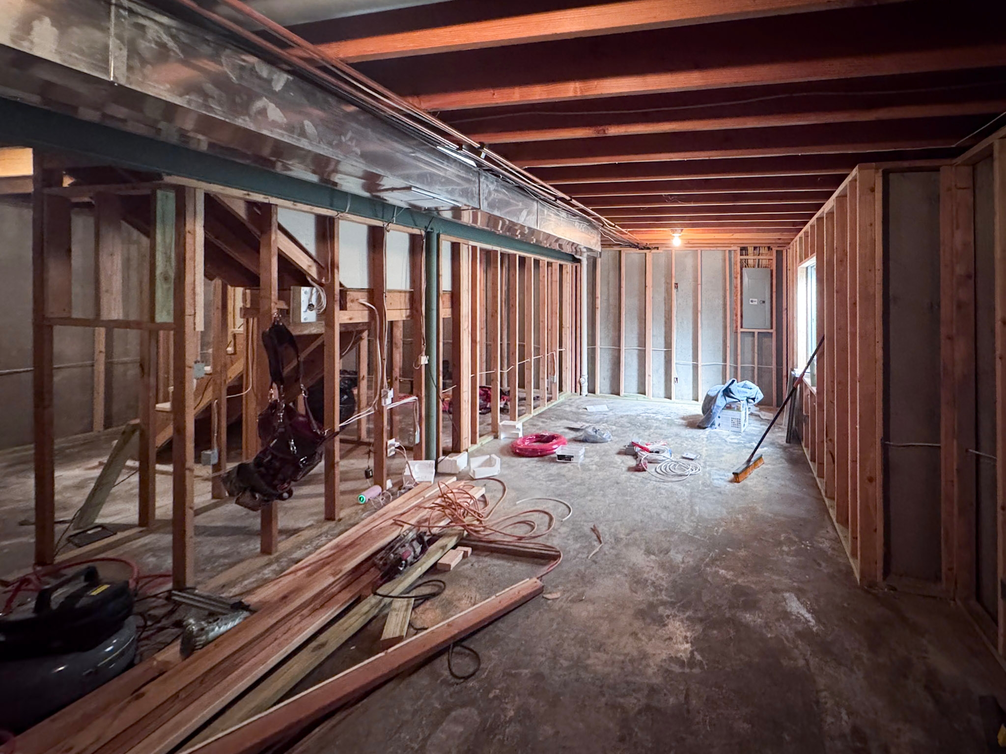 Basement stripped to framing with exposed joists, ductwork, and stud walls during construction