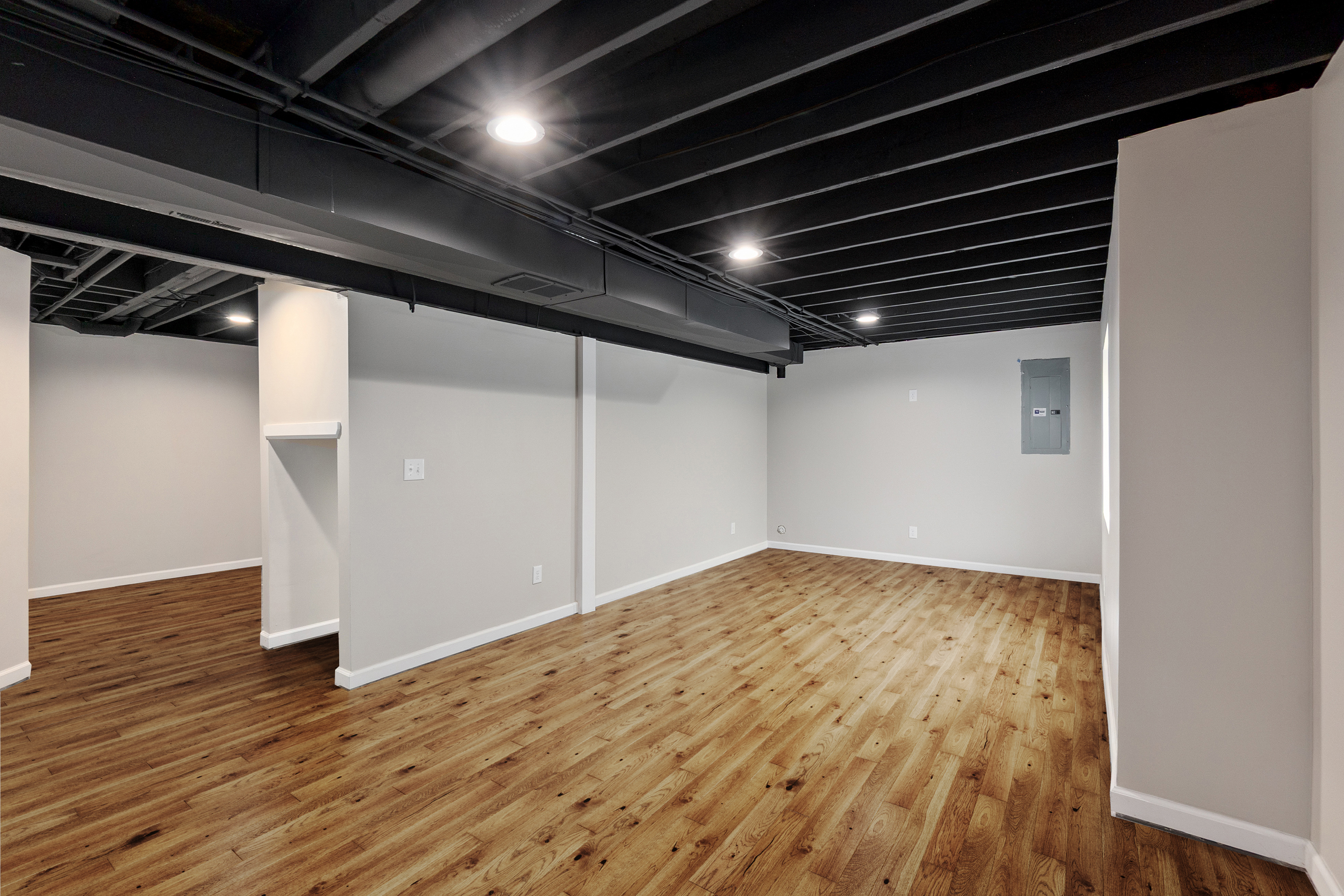 Finished basement living area with wood flooring and a black exposed ceiling